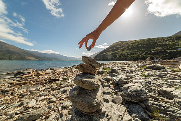 Detail of person stacking rocks by the lake at sunrise. Shot at lake Wanaka, New Zealand.