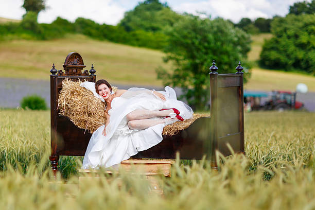 Beautiful happy bride in white dress  having fun on bed in wheat or hay field on summer day. Just married, young amazing woman.