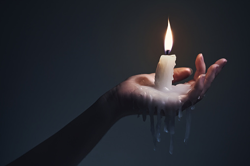 Holding a lit candle that is melting on the hand on a dark background