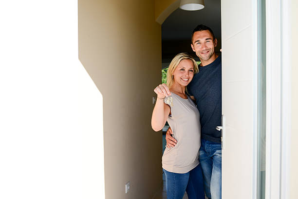 young couple at front door new house showing home key - for rent sign house sign happiness imagens e fotografias de stock