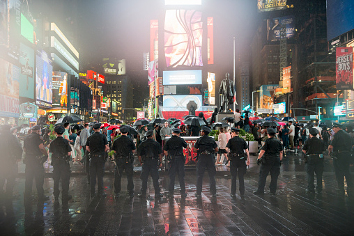 New York City, USA - July 9, 2016: On a wet and rainy night, New York City Police officers stand side by side and watch as Black Lives Matter protestors are gathered in Times Square in New York City, demonstrating against police violence.