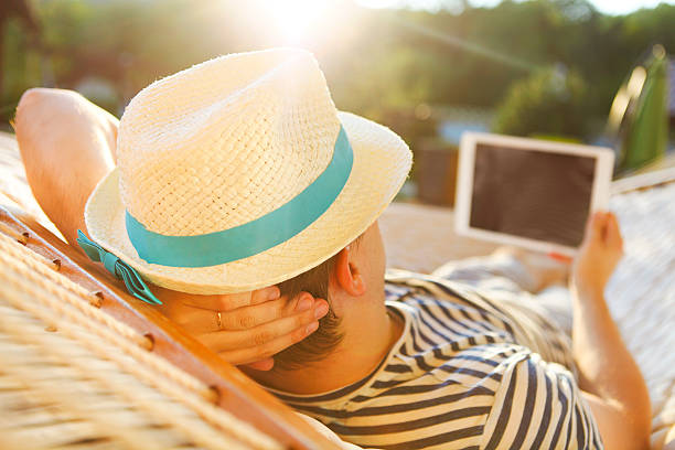 Man in hammock with tablet computer on summer day Lazy time. Man in hat in a hammock with tablet computer on a summer day hammock men lying down digital tablet stock pictures, royalty-free photos & images