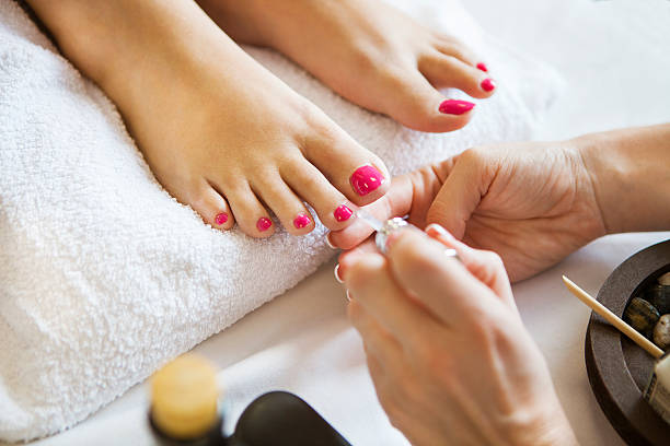 Woman in nail salon receiving pedicure by beautician Woman in nail salon receiving pedicure by beautician. Close up of female feet resting on white towel toenail stock pictures, royalty-free photos & images