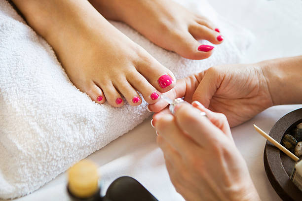 Woman in nail salon receiving pedicure by beautician Woman in nail salon receiving pedicure by beautician. Close up of female feet resting on white towel enamel wear stock pictures, royalty-free photos & images