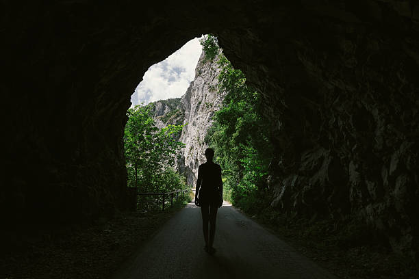 Attractive girl in mini dress standing at exit of old,dark road tunnel. Photo is taken with dslr camera and wide angle lens in European mountains.