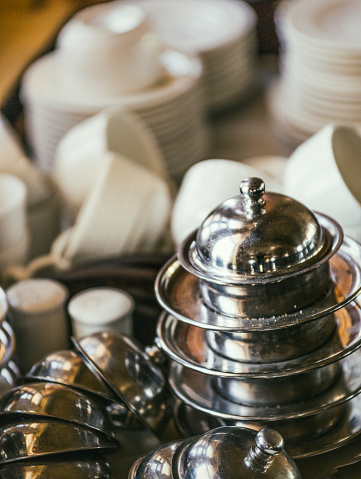 In an Indian restaurant, close-up shot of dishes such as cups, saucers, salt and pepper shakers and small stainless steel serving dish.