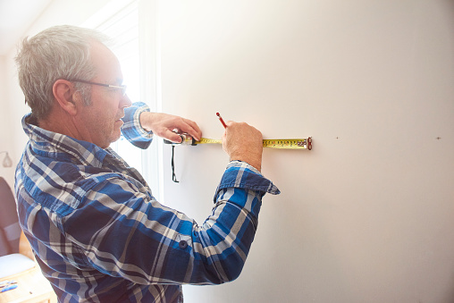 A male is marking out points on a wall ready for his next project. He is working out where each hole should be drilled.