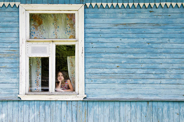 istock Bored little girl looking out window leaning face on hand 546002138