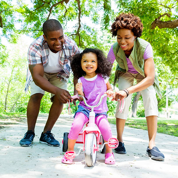 proud parents teach daughter to ride tricycle - family cheerful family with one child texas imagens e fotografias de stock