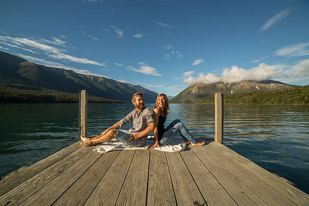 istock Young couple sit back to back on jetty above lake 546008528