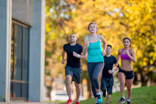 A multi-ethnic group of young adults are running through the city together on a sunny autumn day.