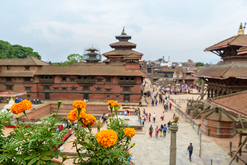 Patan Durbar Square in Nepal. Focus on marigolds, people and building out of focus.