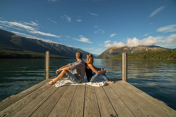 istock Young couple sit back to back on jetty above lake 546020156