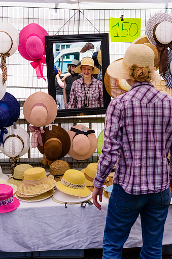 Ronneby, Sweden - July 9, 2016: Big public market day in town with lots of people. Young adult woman trying out a new hat with a big smile in the mirror.