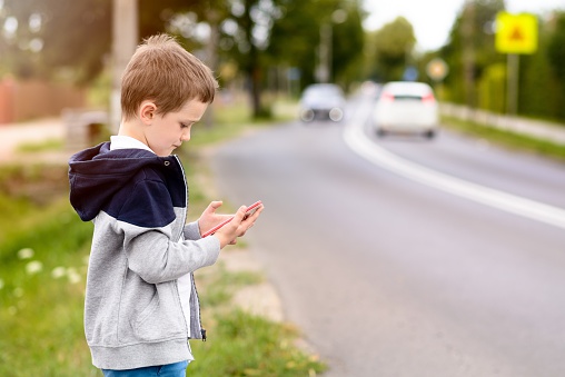 Little boy child playing mobile games on smartphone on the street