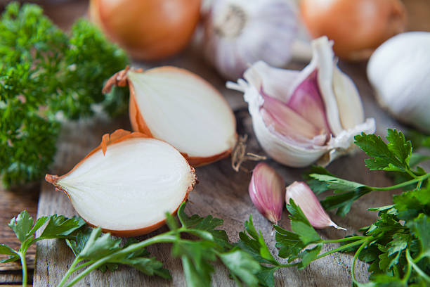 Garlic, onion and shallots on wooden board. Garlic cloves, shallots and white onions   -  food ingredient on wooden board, decorated with  fresh parsley. onion stock pictures, royalty-free photos & images