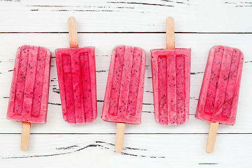Homemade vegan raspberry coconut milk popsicles - ice pops - paletas with chia seeds on rustic white wooden background