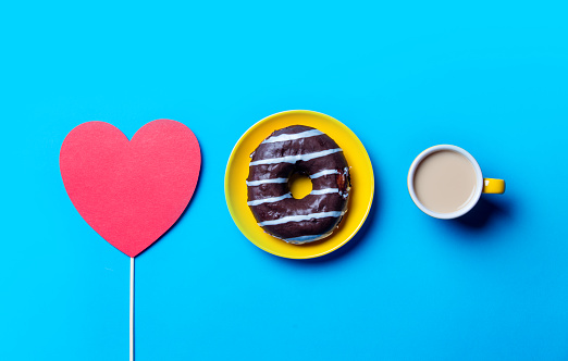 photo of the chocolate donut on the plate,  cup of coffee and red heart shaped toy on the blue background