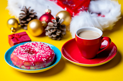 photo of the beautiful Christmas decorations, red cup of coffee and glazed donut on the yellow background