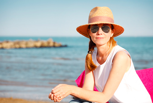 Close-up portrait of smiling female relaxing by the sea. Beautiful mature woman sitting at the seaside and looking at the camera.