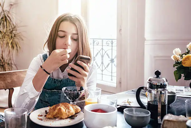 Photo of happy french teenage girl with smartphone at breakfast table