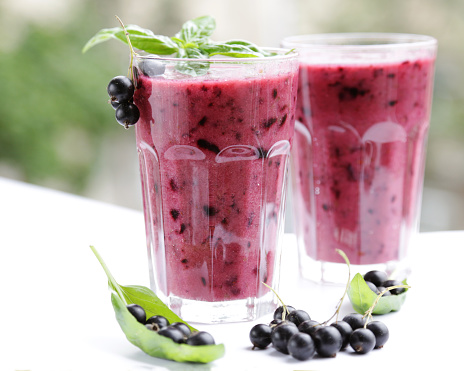 Best Berry Smoothie Drink in Red. Beautiful smoothie, vegan recipe, two glasses, berries, basil green leaves. Summer time 