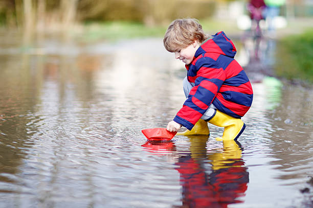 istock Little kid boy playing with paper ship by puddle 546188744