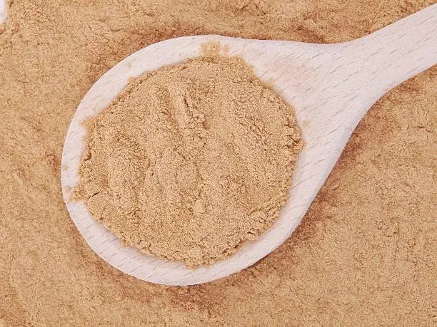 Mesquite powder in wooden spoon over a mesquite heap