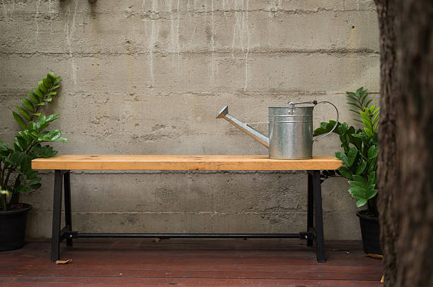 tin watering can on wooden bench with concrete wall in backyard