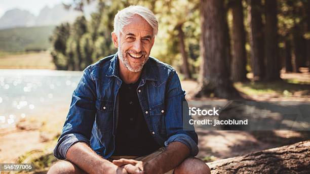 Happy Mature Man Sitting Near A Lake Stock Photo - Download Image Now - Men, Mature Men, Smiling