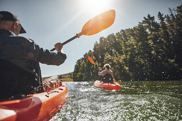 Senior couple kayaking in a lake Outdoor shot of senior man canoeing in the lake with woman in background on a summer day. Man and woman in two different kayaks in the lake on a sunny day. paddling stock pictures, royalty-free photos & images