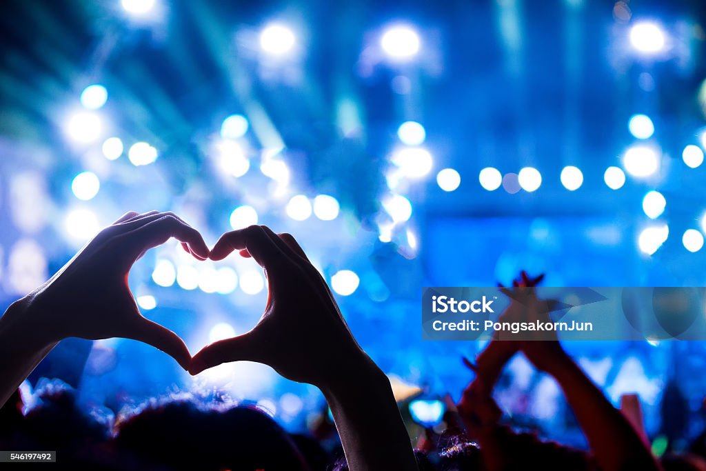 Crowd of Audience at during a concert Crowd of Audience at during a concert with silhouette of a heart shaped hands shadow, light illuminated is power of music concert Music Festival Stock Photo