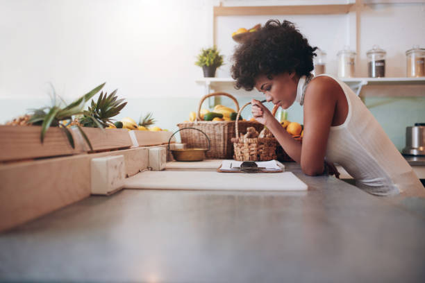 Proprietor of a juice bar calculating a her business expenses Female proprietor of a juice bar calculating a her business expenses. African young woman looking at the clip board on counter. juice bar stock pictures, royalty-free photos & images