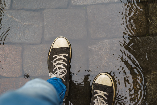 Male legs in sneakers and blue jeans walking through the rain puddle, top view