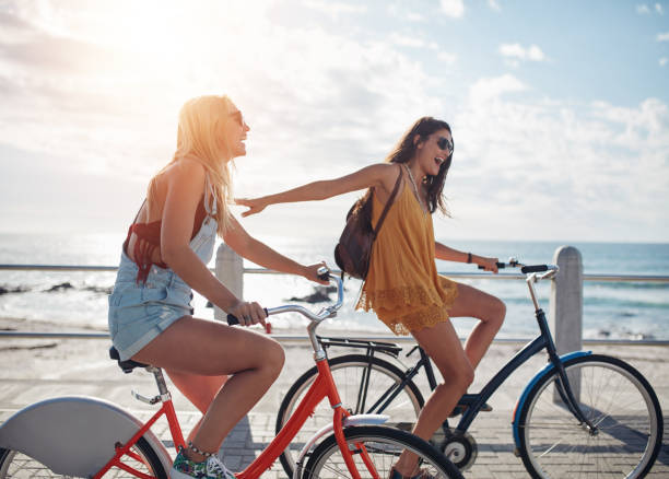 海辺の遊歩道で自転車に乗るために2人の友人 - smart casual outdoors friendship happiness ストックフォトと画像