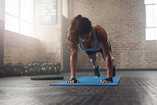 Young muscular woman doing core exercise on fitness mat in the gym. Fit female doing press-ups during the training in the health club.