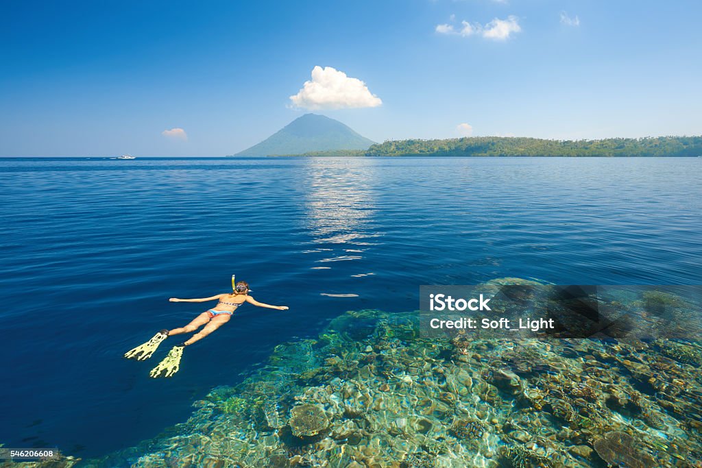 Woman snorkeling in clear tropical waters on background of island Young woman in swimsuit snorkeling in blue and transparent tropical sea on a background volcano Manado Tua.  North Sulawesi, Indonesia. Bunaken Island Stock Photo