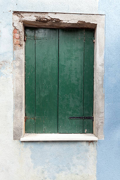 istock Old window with dark green shutters on light blue wall 546209808