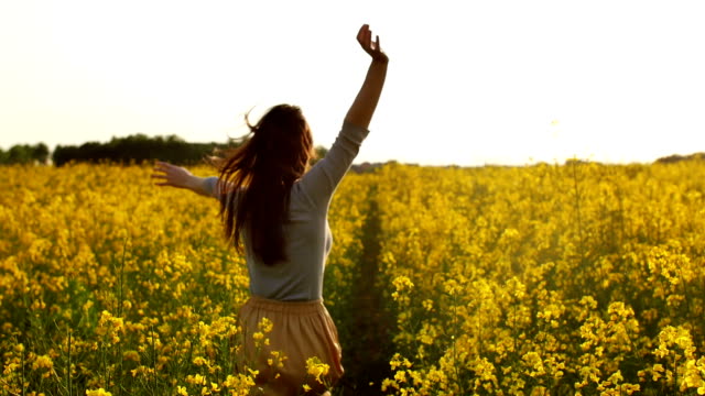 girl runs arms outstretched through a field slowmo