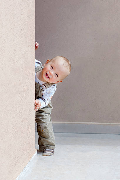 bambino felice che gioca a nascondino e guarda fuori dall'angolo. - photo corner foto e immagini stock