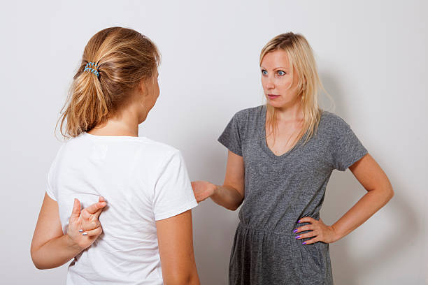 la fille trompe sa mère et croise les doigts derrière son dos. - lying in wait photos et images de collection