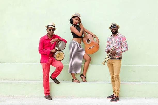 Cuban musical band, the trio consisting of a fairly well-known musicians standing outdoors, on the steps, against the bright green wall. Beautiful young woman standing in the middle, holding a guitar. The man on the left holding the small drums bongos, and a musician on the left holding a trumpet. Havana, Cuba, 50 megapixel image.