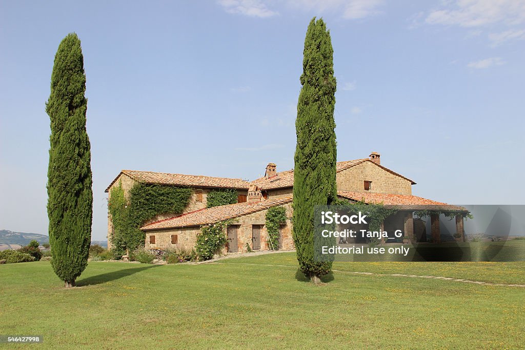 Tuscany Villa with Cypress Trees Pienza, Italy - July 4, 2014: A landscape of a countryside with green grass, cypress trees and typical tuscany farmhouse. Agriculture Stock Photo