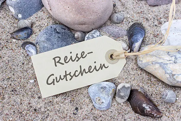Sandy beach with stones and shells and card with German text: travel voucher