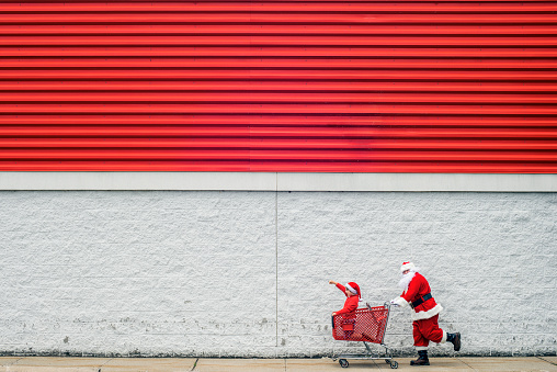 Santa Claus and child sitting in shopping cart rushing to get the best Christmas deals before the season, plenty of season colored copyspace.