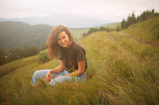 Woman sitting on a grass overlooking the mountains at sunset.