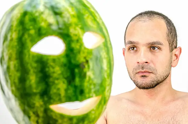 Photo of man holding mask of fruit or watermelon over his face