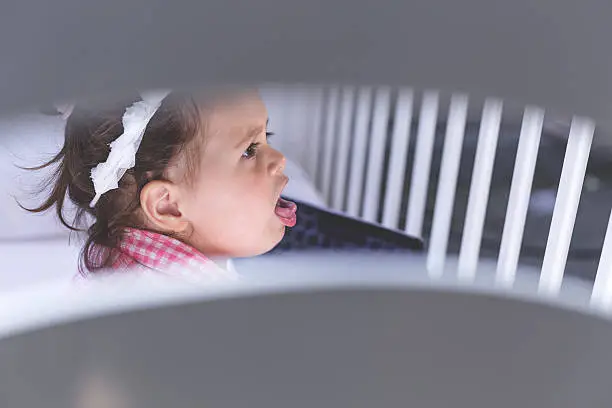 one year old baby is coughing while sitting in a crib beside a laptop  in a plaid shirt