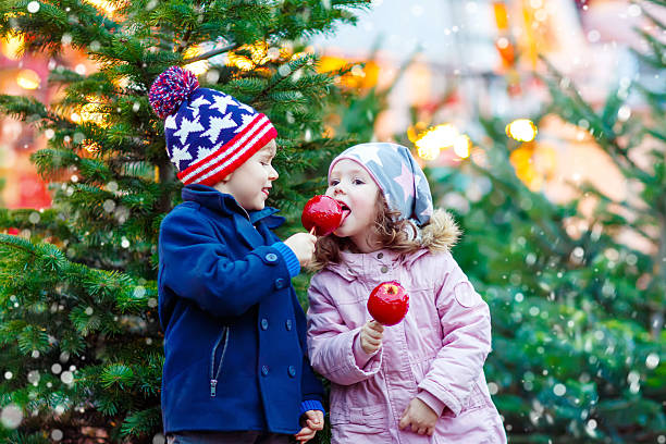 двое маленьких детей едят кристаллизованное яблоко на рождественском рынке - apple eating little girls green стоковые фото и изображения
