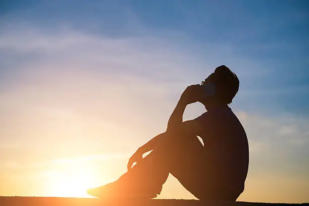 Photo of man talking phone at sunrise